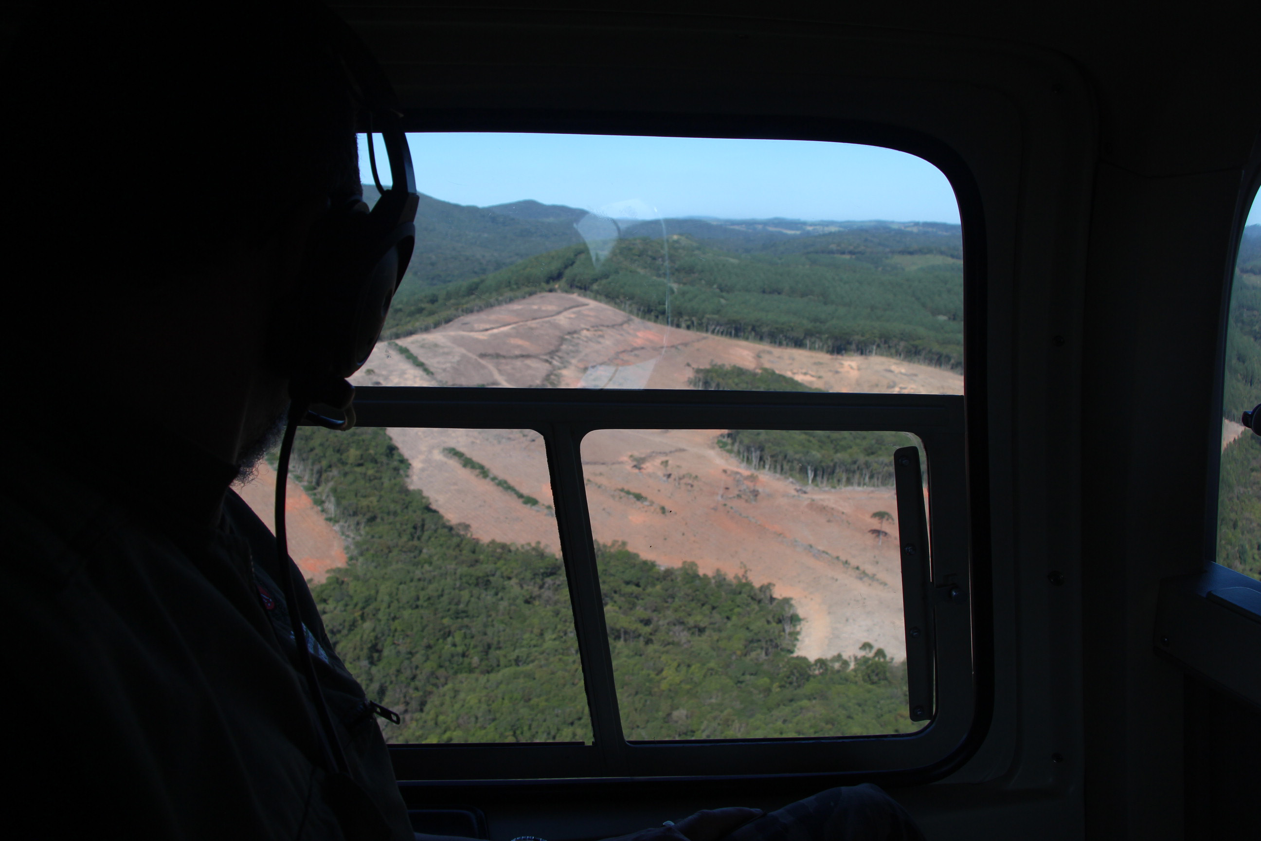 Imagem de dentro do helicoptero para fora, focado na área desmatada