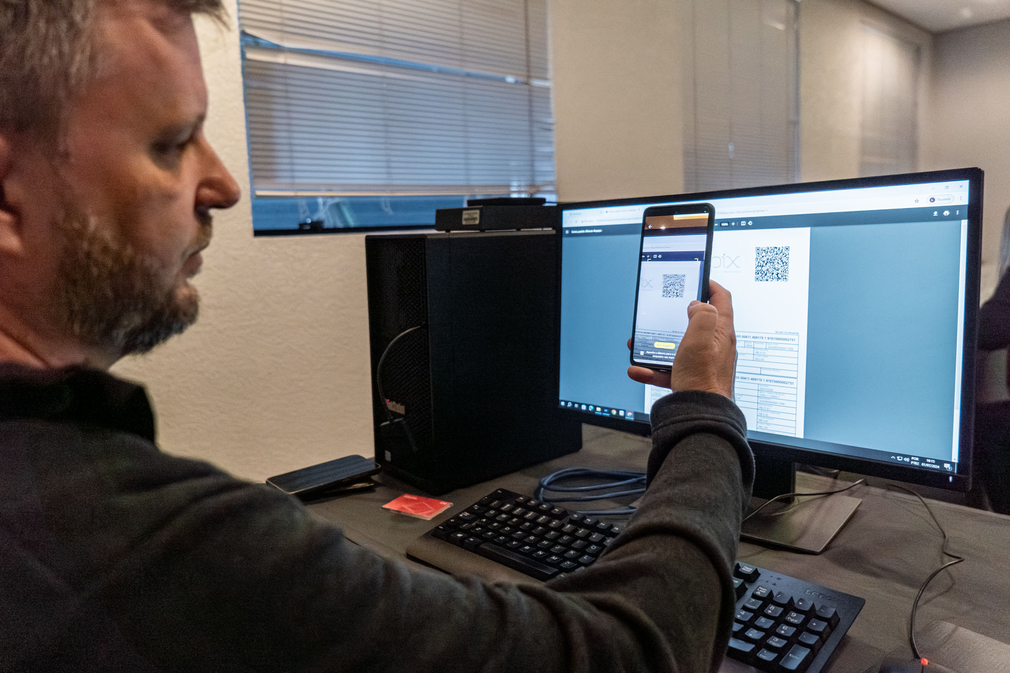 INIDIVÍDUO LENDO UM QR CODE NO COMPUTADOR COM SEU CELULAR