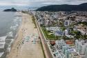 Praia vista de cima, com cidade ao fundo e banhistas de tendas e barracas armadas