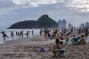 Banhistas apreciando a praia com prédios e um morro ao fundo