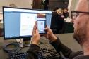 INIDIVÍDUO LENDO UM QR CODE NO COMPUTADOR COM SEU CELULAR