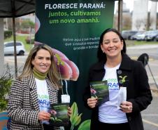 Representante do IAT posando para foto com civil a frente do banner "Florescer Paraná"