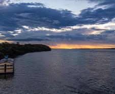 Rio Paraná ao entardecer. Pequena embarcação navegando próxima da margem esquerda.