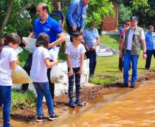 Crianças supervisionadas por adultos soltando os peixes na água