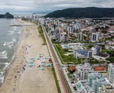 Praia vista de cima, com cidade ao fundo e banhistas de tendas e barracas armadas