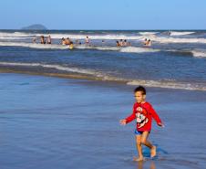 Criança na beira da praia com mar ao fundo