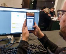INIDIVÍDUO LENDO UM QR CODE NO COMPUTADOR COM SEU CELULAR