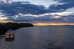 Rio Paraná ao entardecer. Pequena embarcação navegando próxima da margem esquerda.