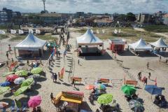 Praia com varios banhistas em torno de barracas e guarda-sois