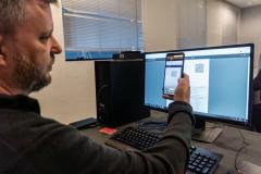 INIDIVÍDUO LENDO UM QR CODE NO COMPUTADOR COM SEU CELULAR