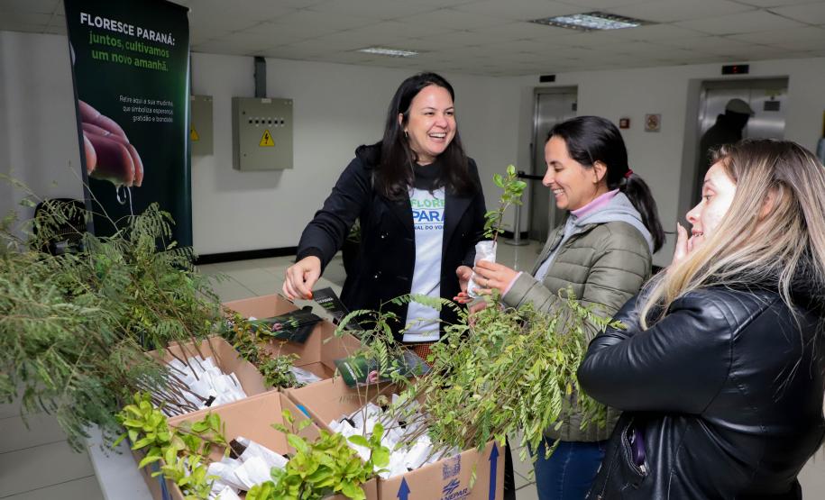 Representantes do IAT posando para foto com civis a frente do banner "Florescer Paraná"