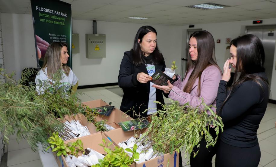 Representantes do IAT posando para foto com civis a frente do banner "Florescer Paraná"