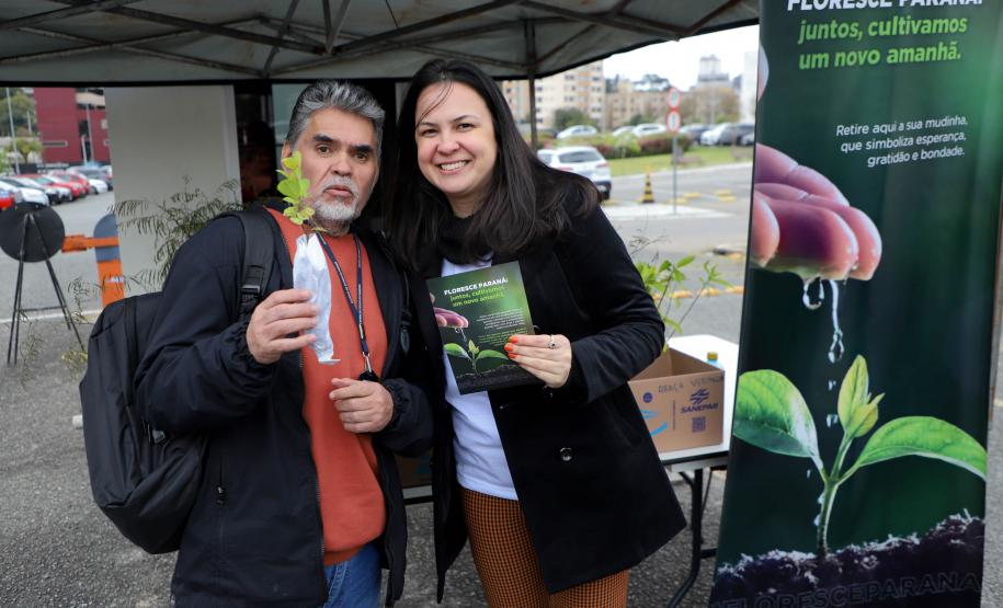 Representante do IAT posando para foto com civil a frente do banner "Florescer Paraná"
