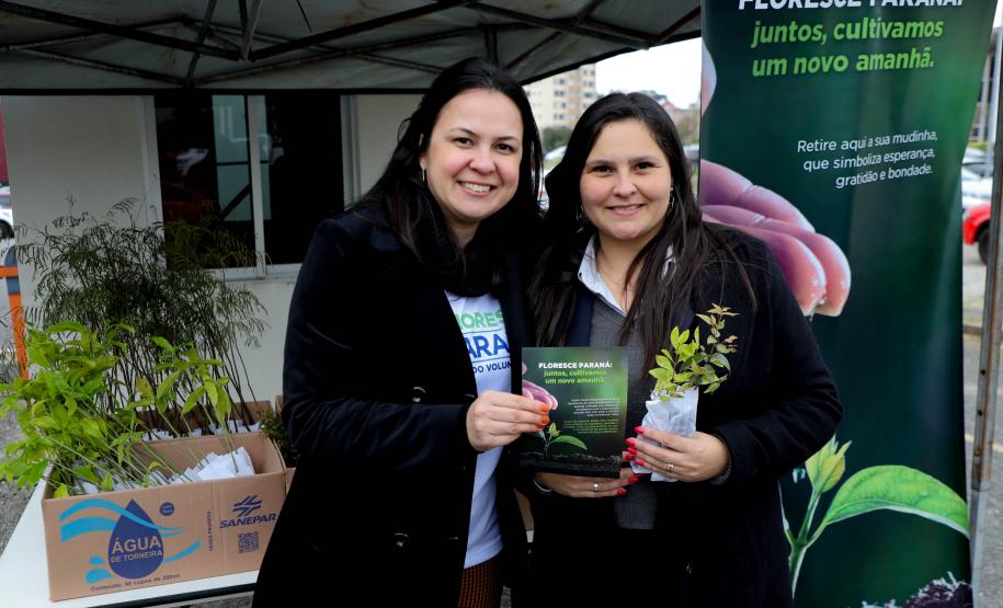Representante do IAT posando para foto com civil a frente do banner "Florescer Paraná"