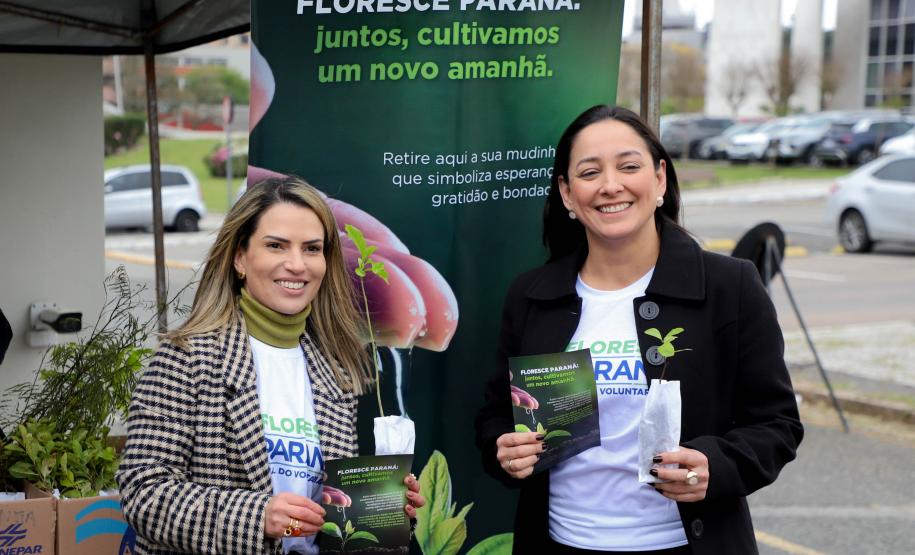Representante do IAT posando para foto com civil a frente do banner "Florescer Paraná"