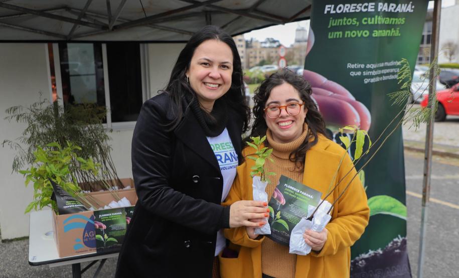 Representante do IAT posando para foto com civil a frente do banner "Florescer Paraná"