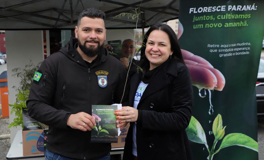 Representante do IAT posando para foto com civil a frente do banner "Florescer Paraná"