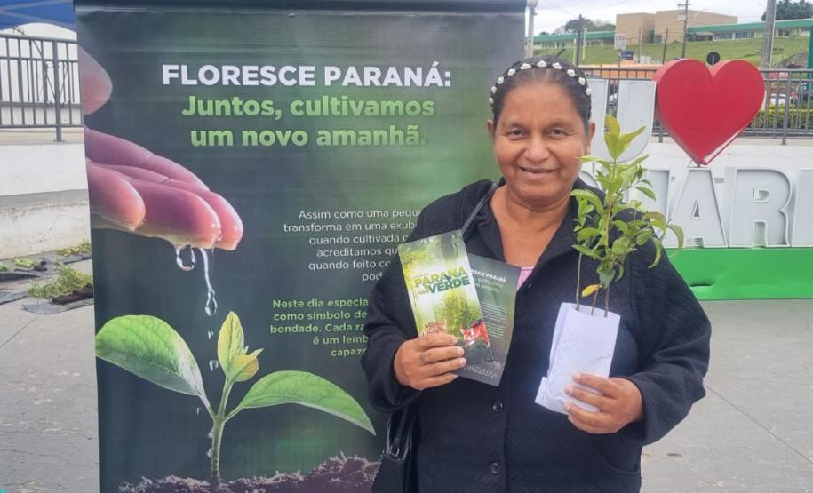 Civil com muda posando para foto a frente do banner "Florescer Paraná"