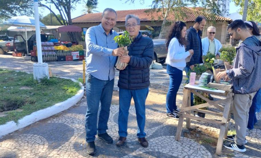 Representante do IAT entregando muda para um civil ao lado do estande.