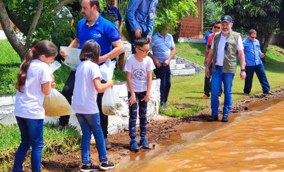 Crianças supervisionadas por adultos soltando os peixes na água