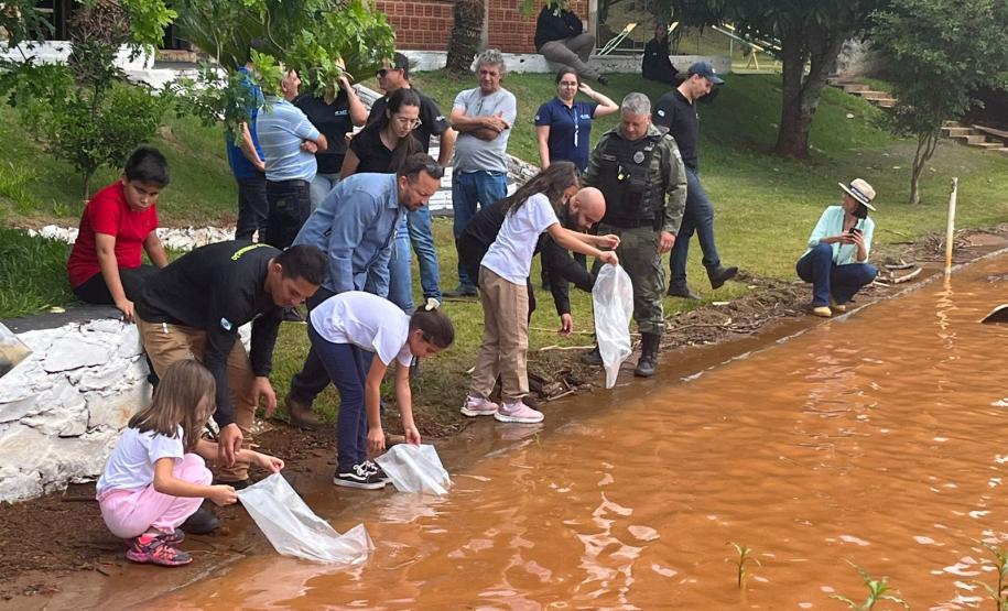 Crianças supervisionadas por adultos soltando os peixes na água