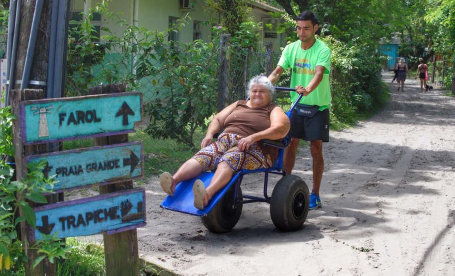 Voluntário transportando idosa em uma cadeira de rodas pelo litoral