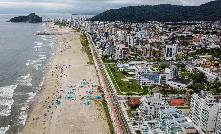 Praia vista de cima, com cidade ao fundo e banhistas de tendas e barracas armadas