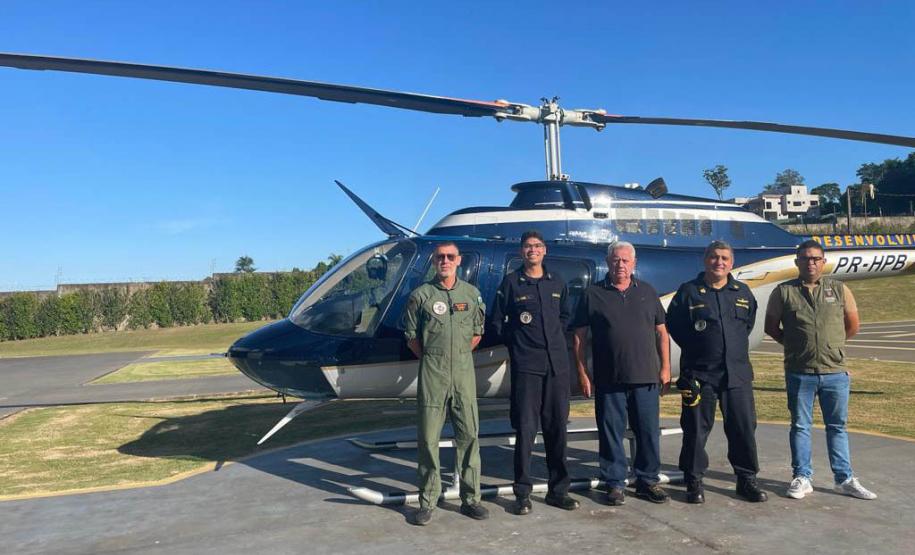 Agentes fiscalizadores posando para foto com um helicóptero ao fundo