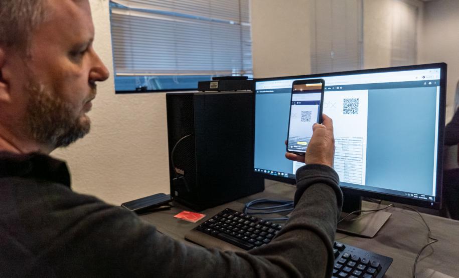 INIDIVÍDUO LENDO UM QR CODE NO COMPUTADOR COM SEU CELULAR