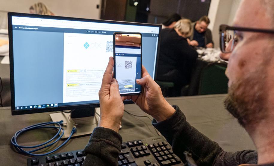 INIDIVÍDUO LENDO UM QR CODE NO COMPUTADOR COM SEU CELULAR